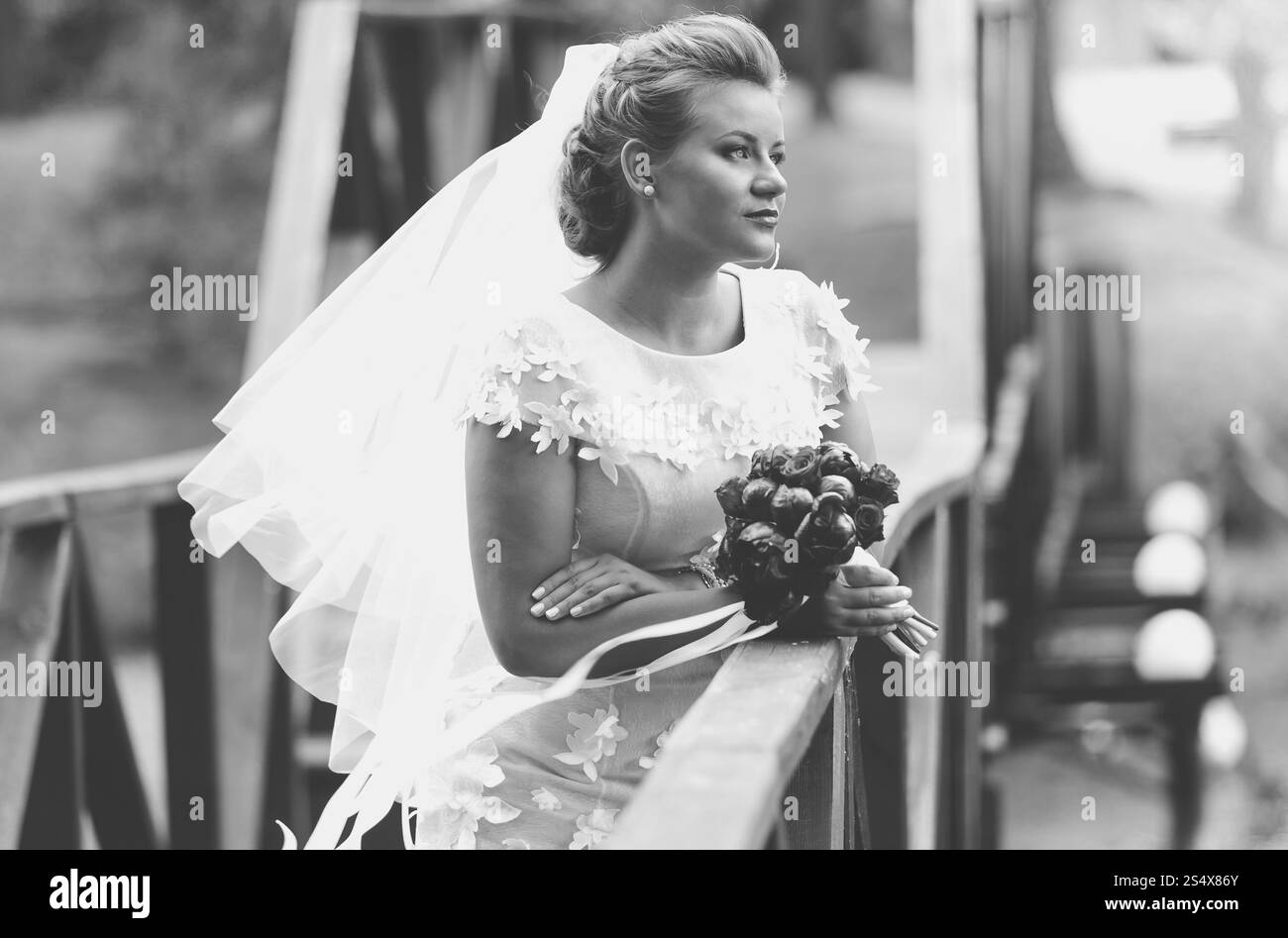 Schwarz-weiß-Porträt einer eleganten Braut, die an windigen Tagen auf einer Holzbrücke posiert Stockfoto