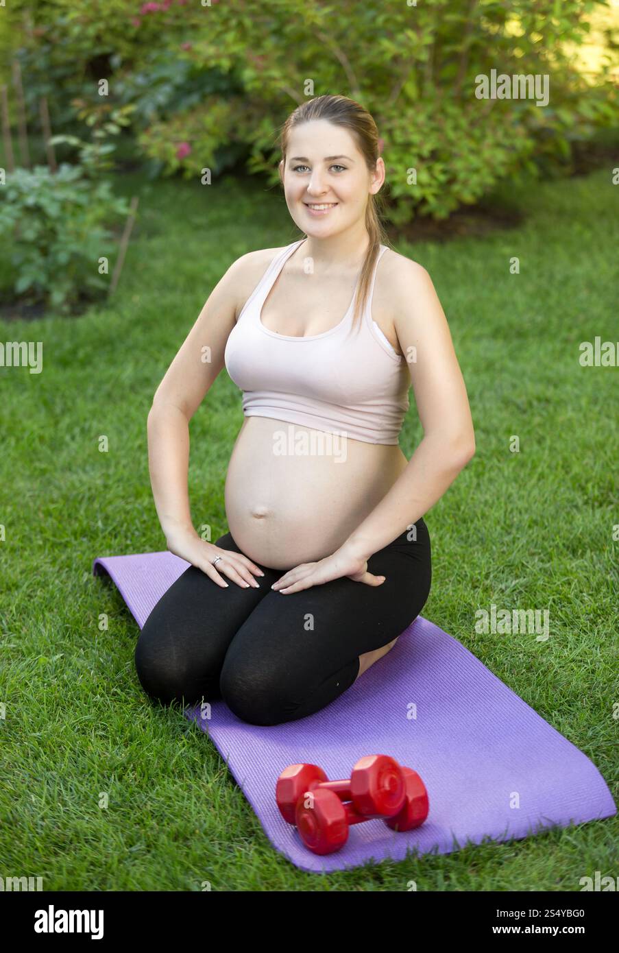 Schwangere Frau, die sich am sonnigen Tag im Park auf dem Gras ausdehnt Stockfoto