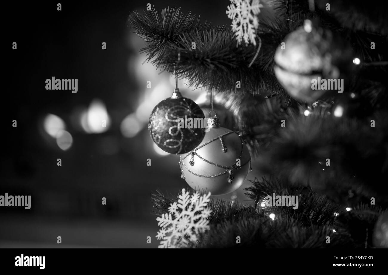 Schwarz-weiß-Aufnahme von wunderschön dekoriertem Weihnachtsbaum vor dem brennenden Kamin im Haus. Konzentrieren Sie sich auf den Kamin Stockfoto