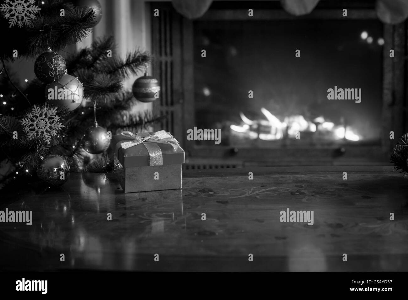 Schwarz-weißer Hintergrund mit Holztisch vor brennendem Kamin und Weihnachtsbaum Stockfoto