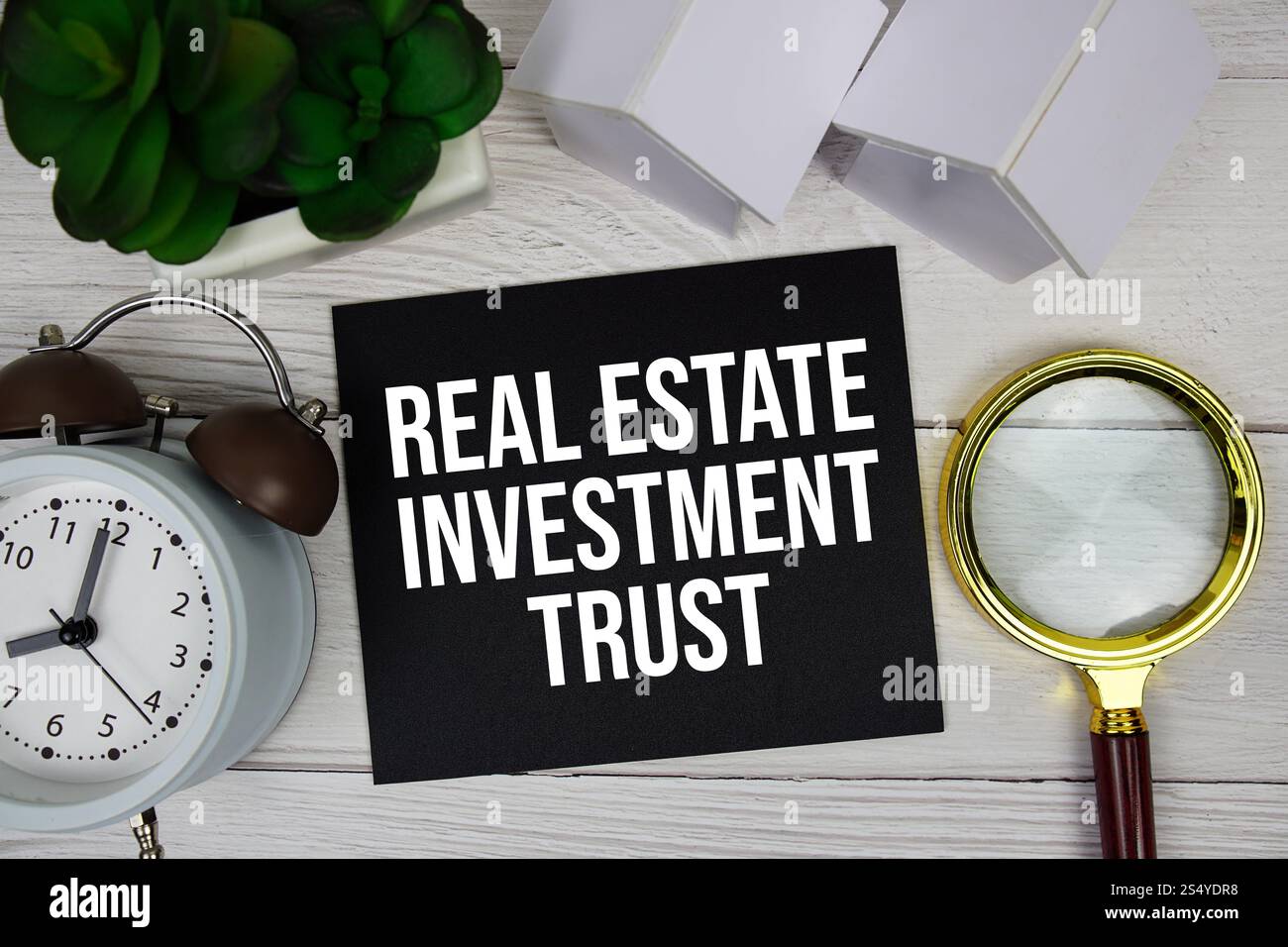 Real Estate Investment Trust Textnachricht auf Haftnotiz mit Wecker, Lupe und Hausmodell auf Holzhintergrund Stockfoto