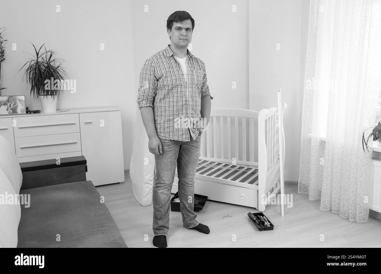 Schwarz-weiß-Bild eines jungen Mannes, der im Schlafzimmer posiert, mit zerlegten Möbeln Stockfoto