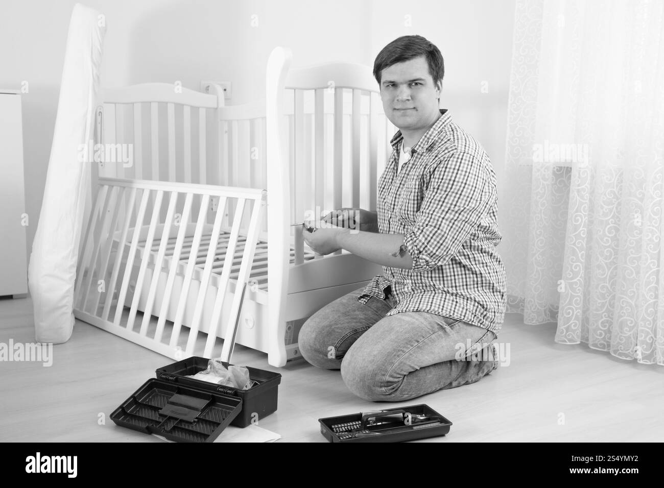 Schwarz-weiß-Foto eines Handwerkers, der auf dem Boden sitzt und Möbel zusammenbaut Stockfoto