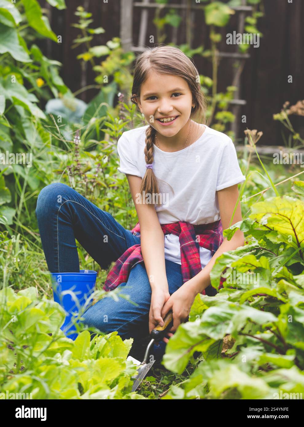 Lächelndes Mädchen, das im Garten arbeitet und frischen grünen Salat ausgräbt Stockfoto