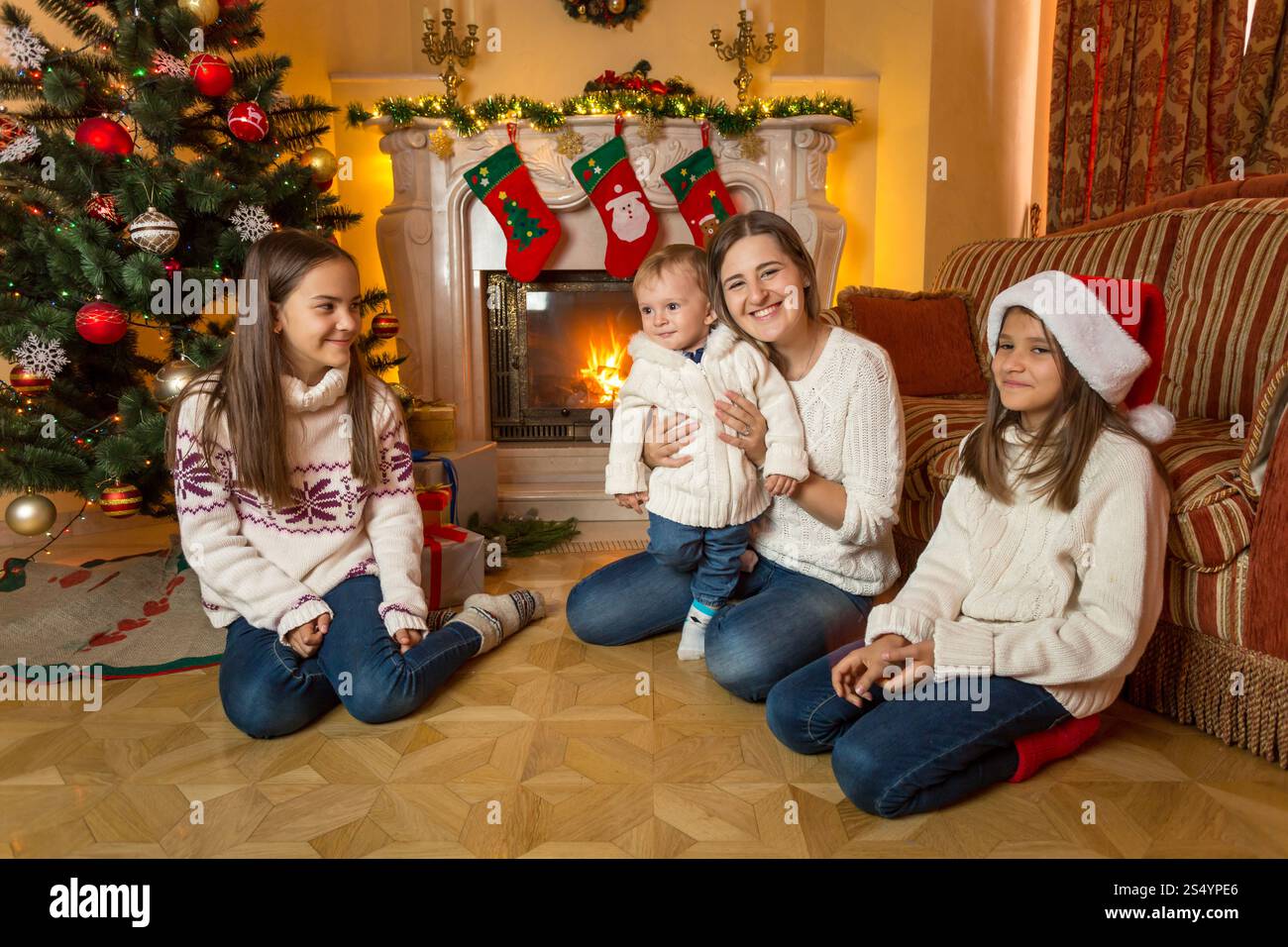 Mutter, Sohn und zwei Töchter auf der Etage neben dem Kamin an Weihnachten Stockfoto
