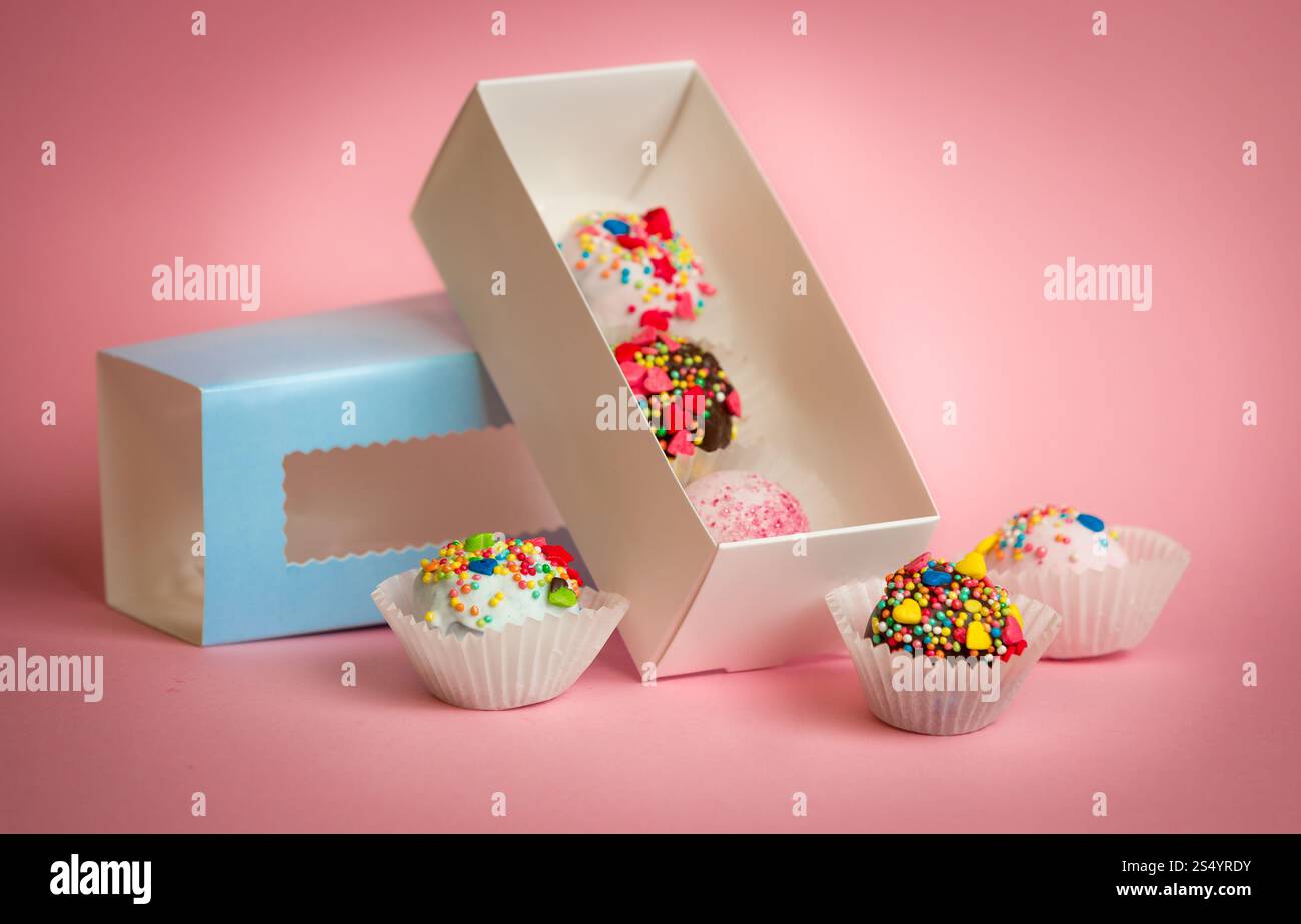 Offene Box mit hausgemachten Kuchenbällchen mit bunten Streuseln auf rosa Hintergrund Stockfoto