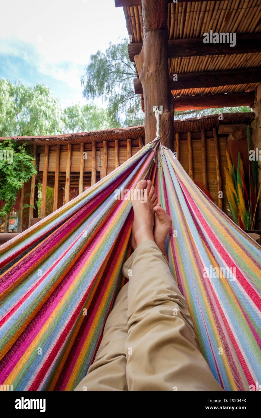 Ein Mann, der sich in einer farbigen Hängematte entspannt. Subjektive Sicht. Entspannen Sie in der Hängematte Stockfoto
