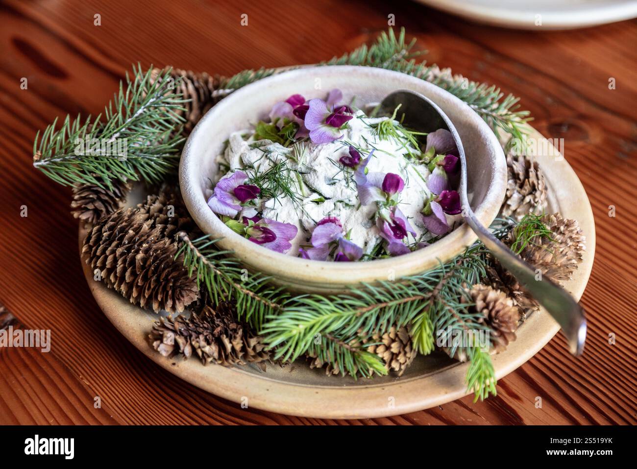 Wunderschönes Gericht mit Joghurt, essbaren Blumen und Waldelementen auf einem rustikalen Tisch Stockfoto