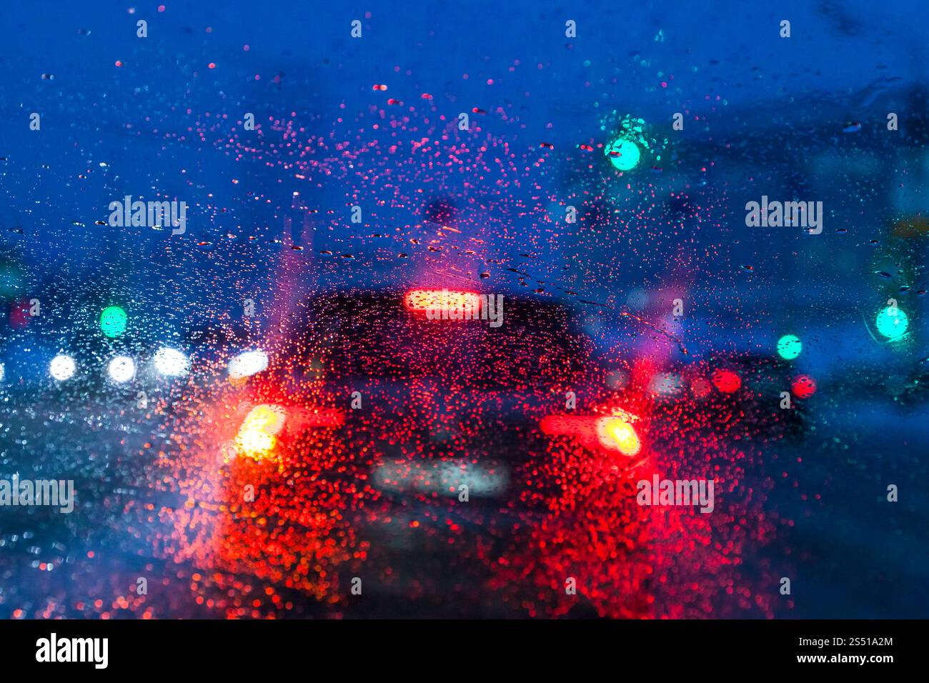Fahren bei nächtlichem Schneefall in Moskau - unscharfer Hintergrund mit Blick durch schmelzenden Schnee auf der Windschutzscheibe des Autos am Winterabend (Fokus auf Wassertropfen Stockfoto