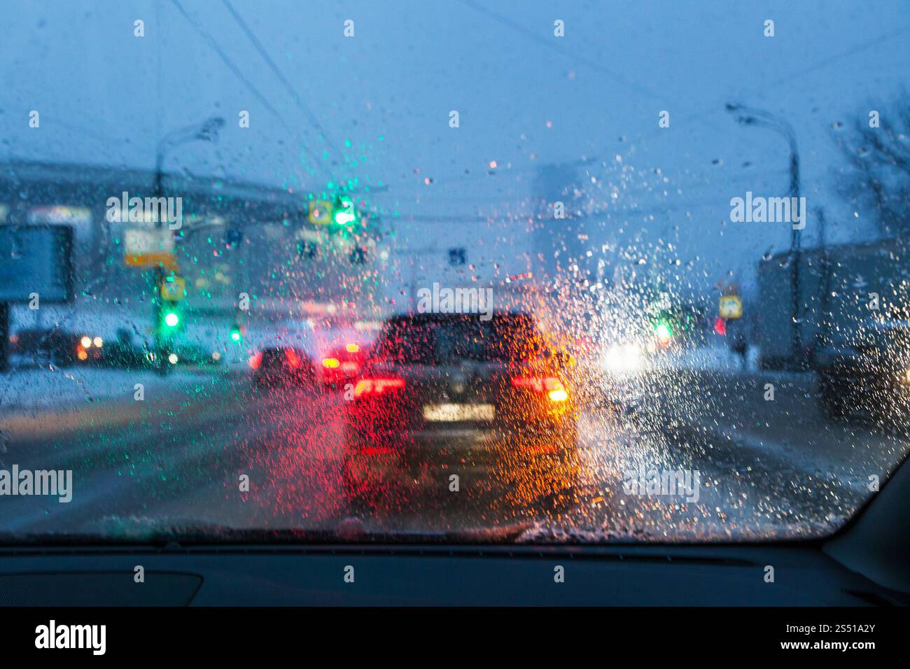 Fahren bei nächtlichem Schneefall in Moskau - verschwommener Hintergrund mit Blick durch Tropfen von schmelzendem Schnee auf der Windschutzscheibe am Winterabend Stockfoto
