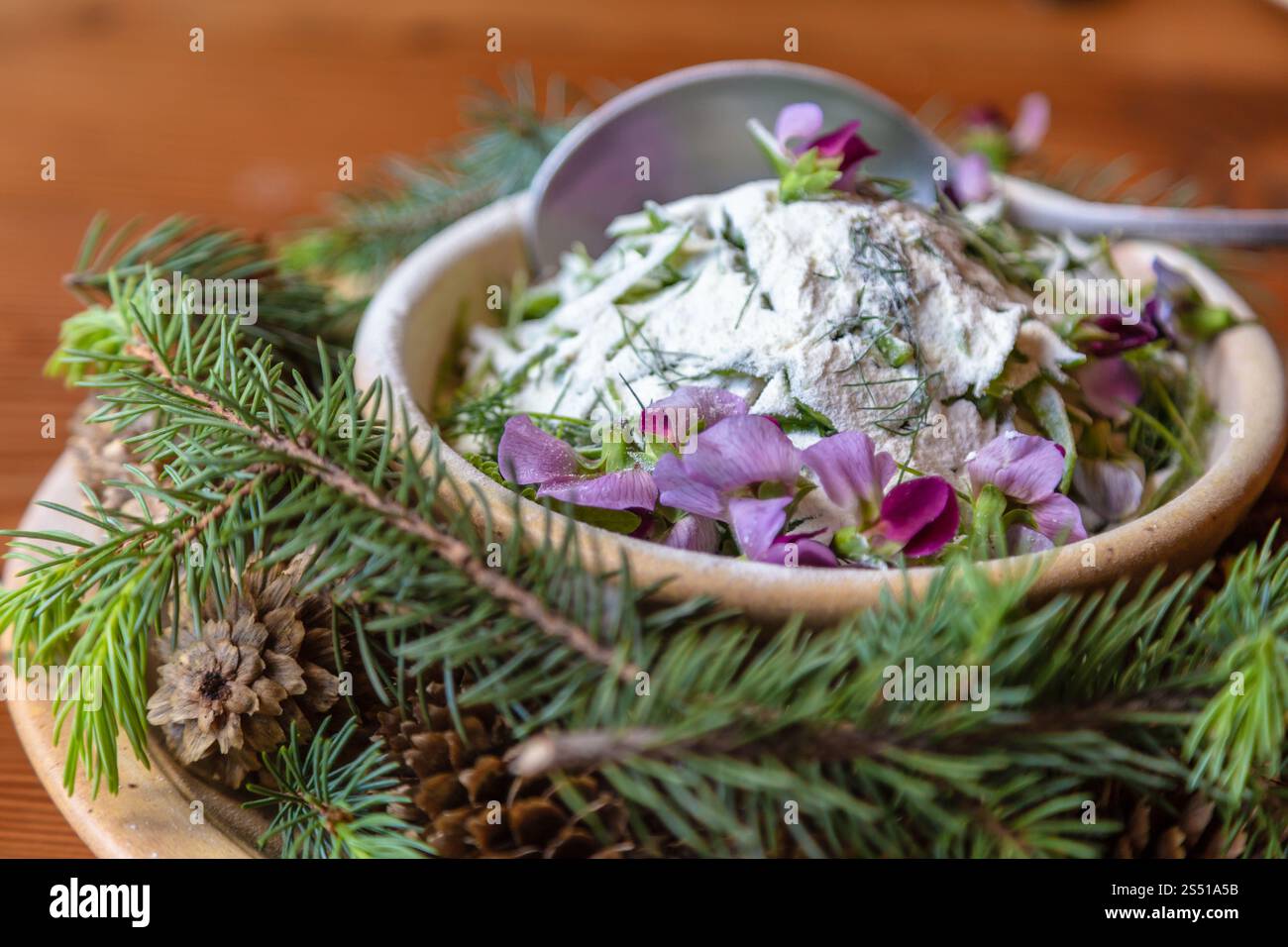 Wunderschönes Gericht mit Joghurt, essbaren Blumen und Waldelementen auf einem rustikalen Tisch Stockfoto