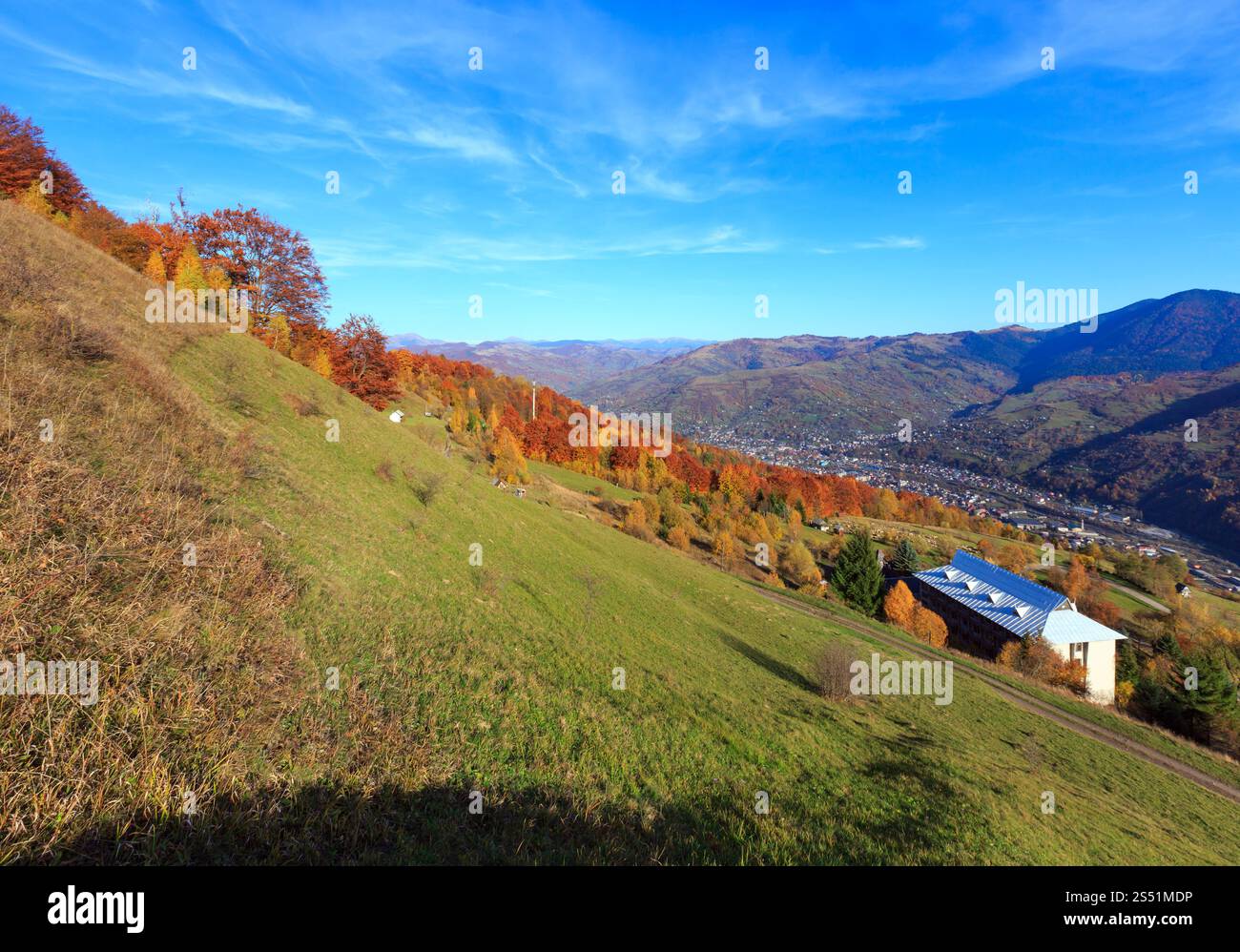 Herbstkarpaten Landschaft mit mehrfarbigen gelb-orange-rot-braunen Bäumen am Hang und Rakhiv Stadt und Tysa Fluss weit unten (Blick von Stockfoto