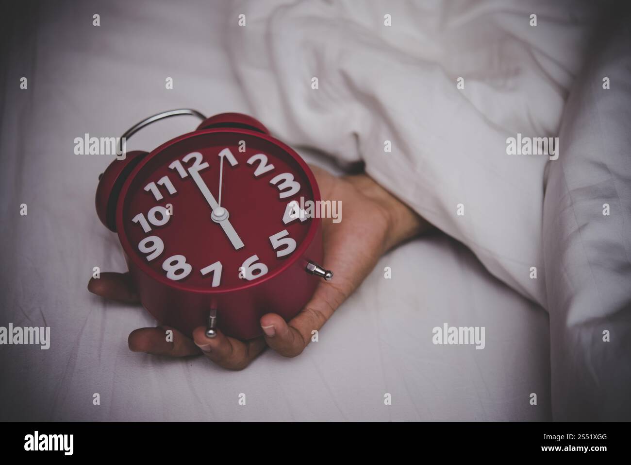 Mann im Bett, der den Wecker auf 6 Uhr stellt. Stockfoto