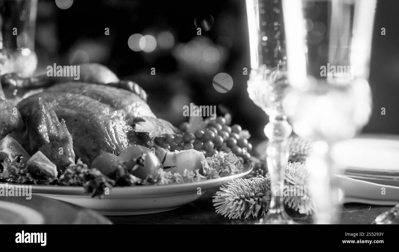 Schwarz-weiß-Foto von gebackenem Huhn und Gläsern mit Champagner auf festlichem Esstisch. Schwarz-weiß-Bild von gebackenem Huhn und Gläsern mit Stockfoto
