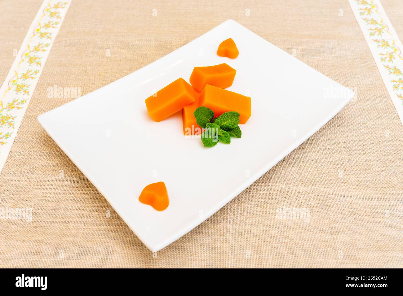 Leuchtend orange Kürbisstücke, die künstlerisch auf einem eleganten weißen Teller platziert und mit frischen Minzblättern garniert werden, sorgen für eine ansprechende kulinarische Präsentation Stockfoto