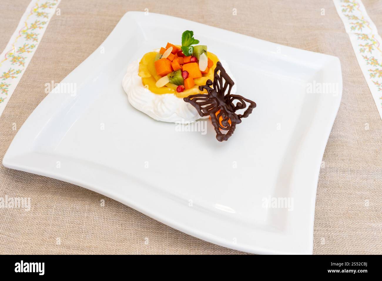 Ein köstliches Dessert besteht aus einer leichten Creme-Basis mit Mango, Kiwi und bunten geschnittenen Früchten. Ein zarter Schokoladenschokolade-Schmetterling verleiht ihm eine künstlerische Note Stockfoto