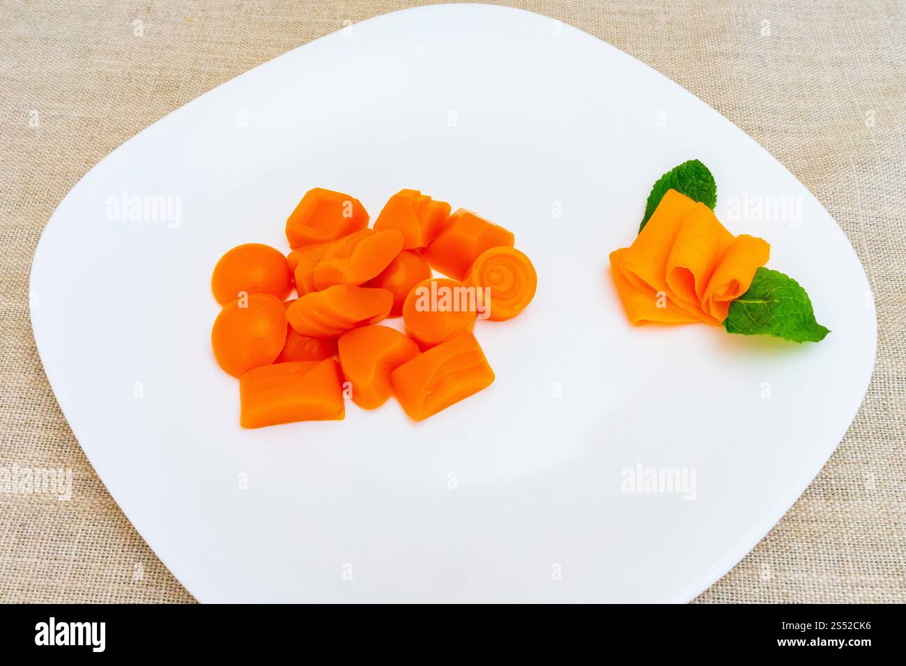 Leuchtend orange Karottenstücke sind kreativ auf einer weißen Platte angeordnet. Einige Stücke sind wie Blumen und Bänder geformt und zeigen künstlerische kulinarische Prägung Stockfoto