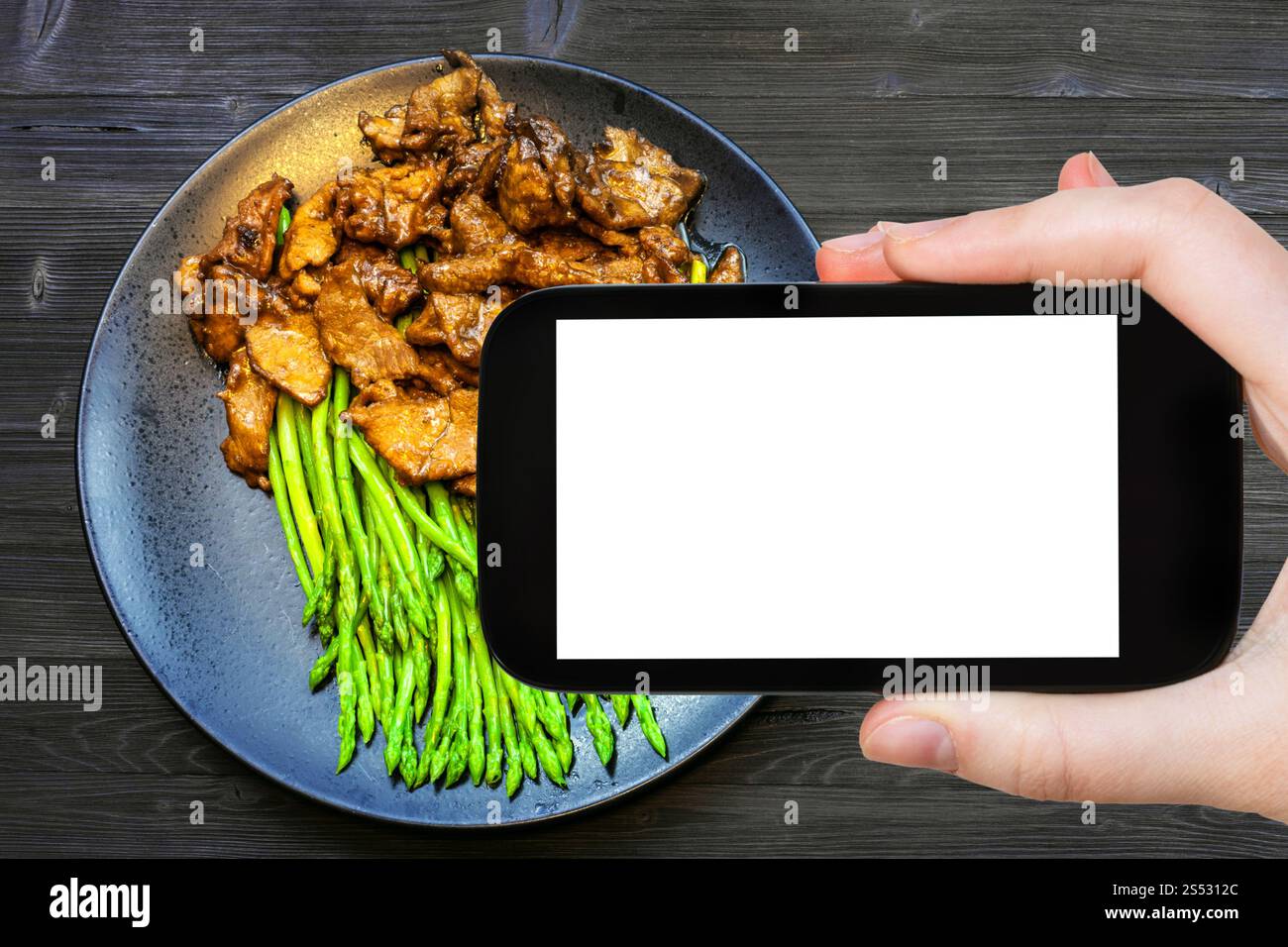 Reisekonzept - Touristenfotos von chinesischem Rindfleisch in Sojasauce mit grünem Spargel auf dem Smartphone mit leerem Bildschirm Stockfoto