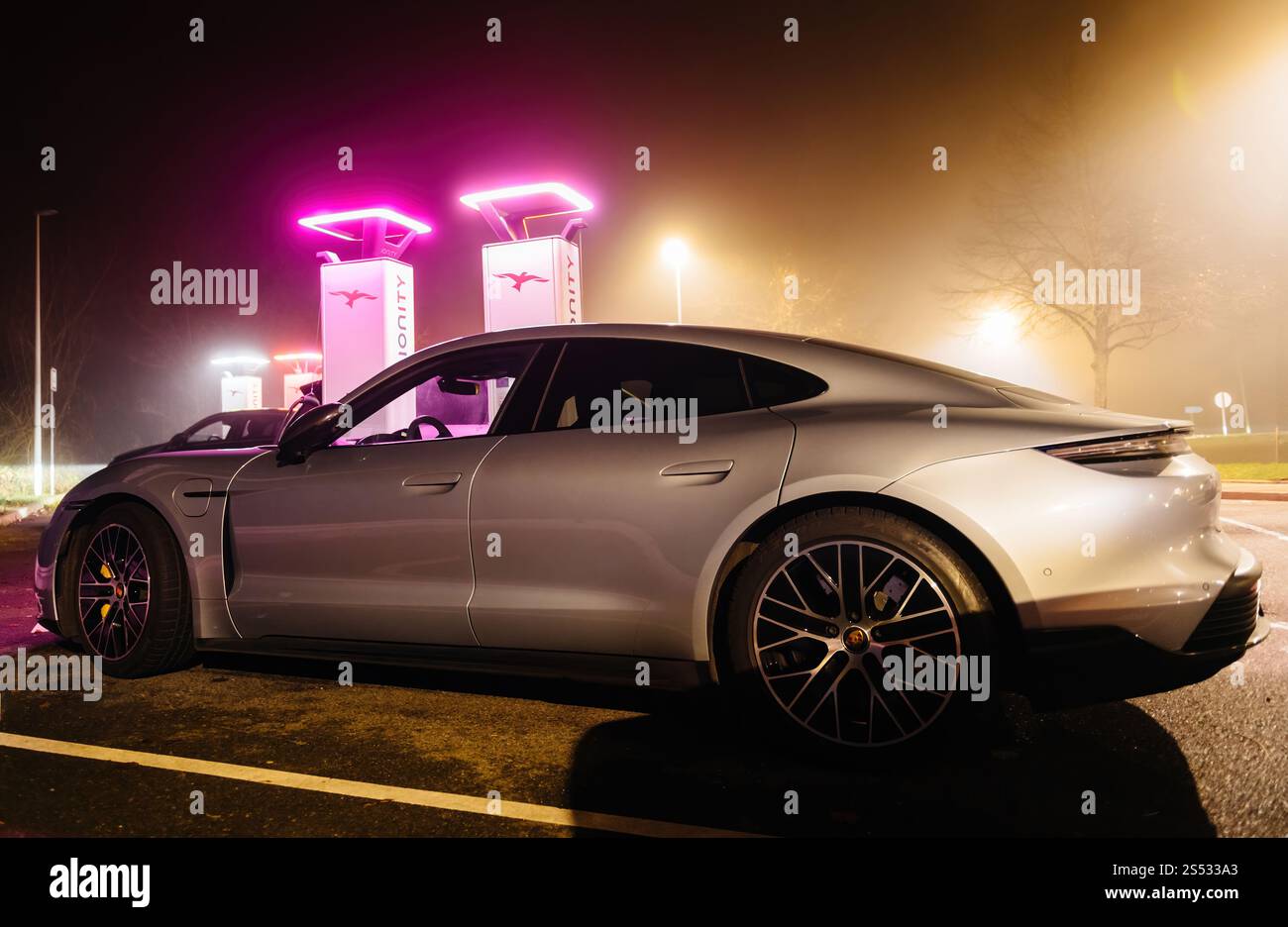 Brumath, Frankreich - 26. Dezember 2024: Ein elegantes silbernes Elektroauto lädt an einer Ionity-Station mit leuchtenden rosa Lichtern vor nebeliger Kulisse auf Stockfoto