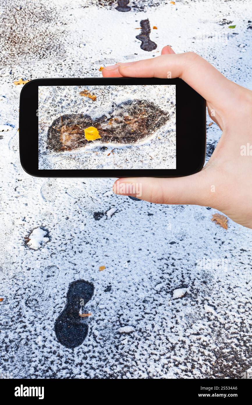 Travel Concept - touristische Fotografien von gefrorenen Fußabdrücke auf nasser Fahrbahn mit dem ersten Schnee in kalten Herbsttag auf dem Smartphone in Moskau, Russland Stockfoto
