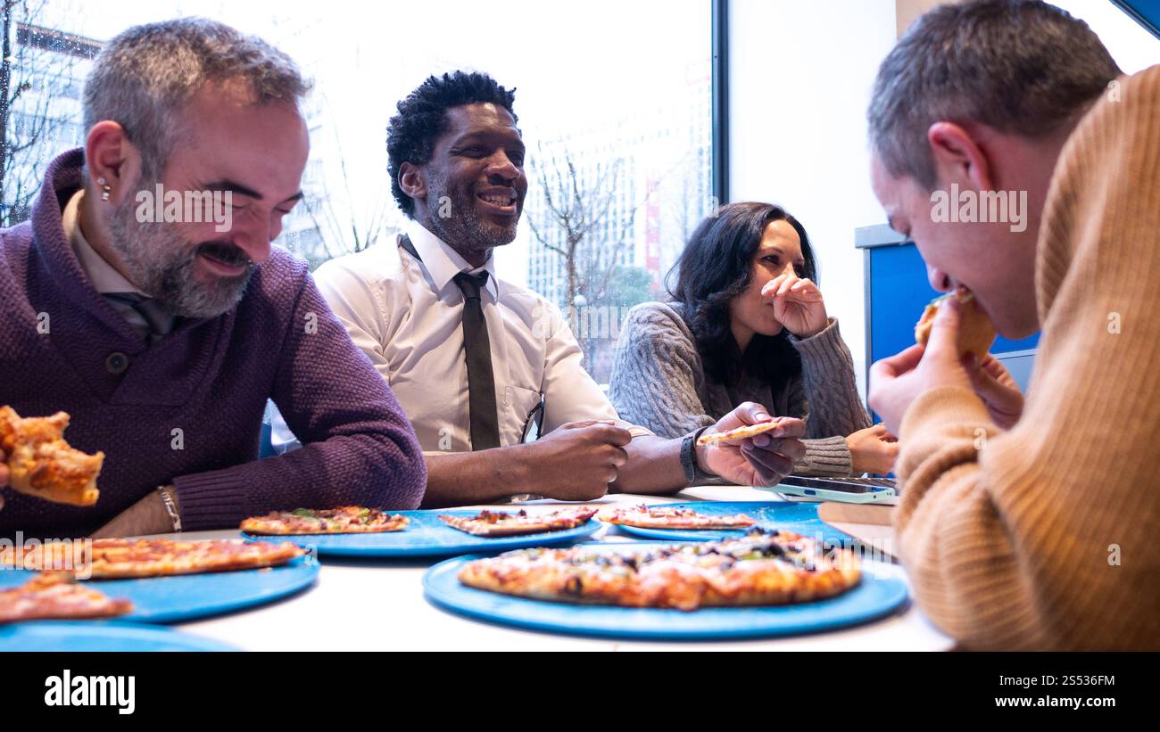 Eine Gruppe verschiedener Kollegen genießt Pizza und lacht zusammen Stockfoto