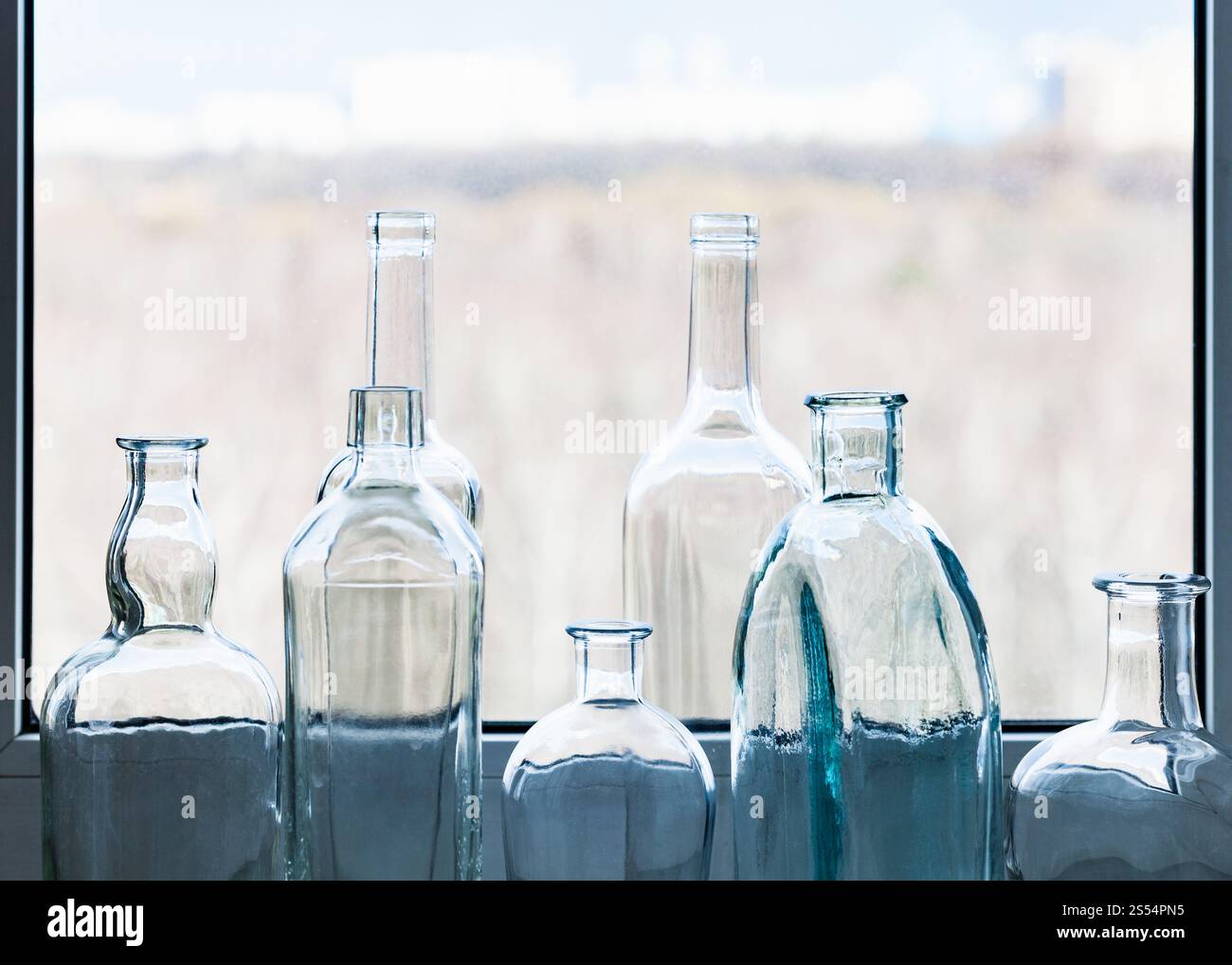 Viele leere betrunkene Flaschen und Blick auf den Stadtpark durch das Fenster am sonnigen Frühlingstag im Hintergrund. Leere Flaschen und Blick auf den Stadtpark durch Stockfoto