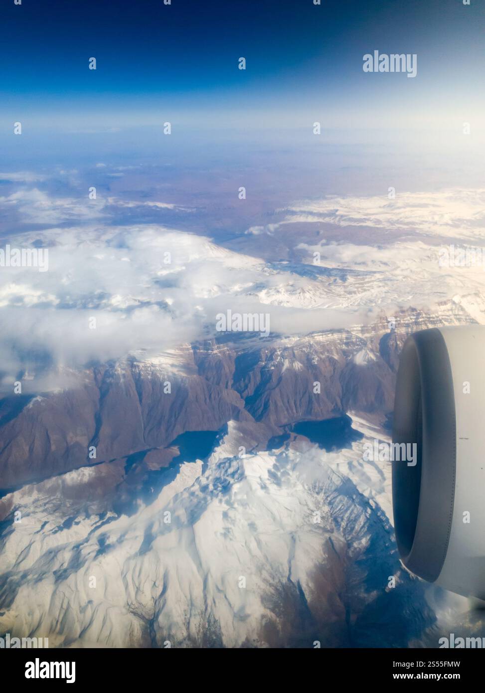Blick vom Bullauge des Flugzeugs auf den Motor und die mit Schnee bedeckten Gipfel. Blick vom Bullauge des Flugzeugs auf den Motor und die Bergspitzen mit bedeckt Stockfoto