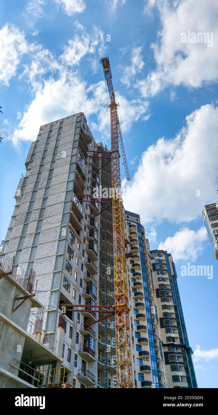 Foto des Hochbaukrans auf der Baustelle des neuen modernen Viertels vor blauem Himmel mit weißen Wolken. Bild: Hochbaukran an Stockfoto