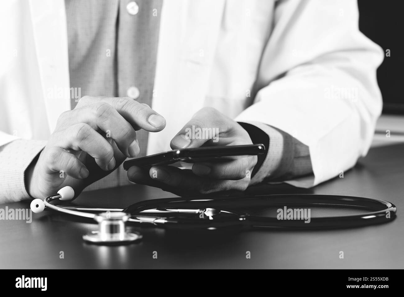 Nahaufnahme von smart Arzt arbeiten mit Smartphone und Stethoskop auf dunklen Schreibtisch aus Holz, schwarz / weiß Stockfoto