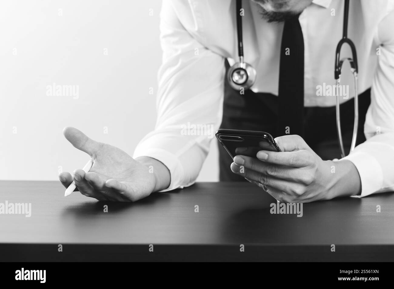 Nahaufnahme von smart Arzt arbeiten mit Smartphone und Stethoskop auf dunklen Schreibtisch aus Holz, schwarz / weiß Stockfoto