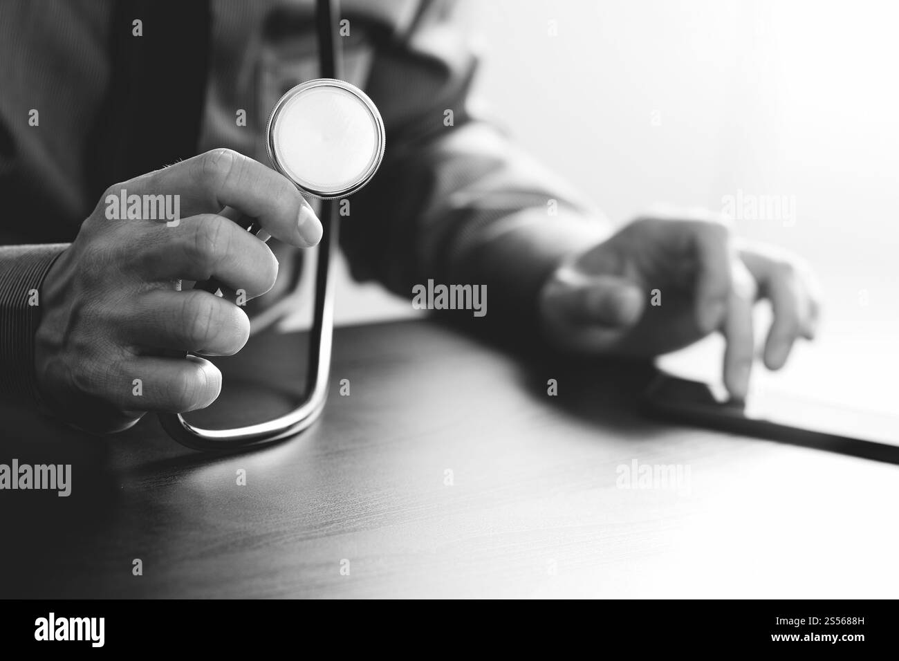 Nahaufnahme von smart Arzt arbeitet mit Stethoskop und Handy auf dunklen Holz Schreibtisch im modernen Krankenhaus, schwarz / weiß Stockfoto