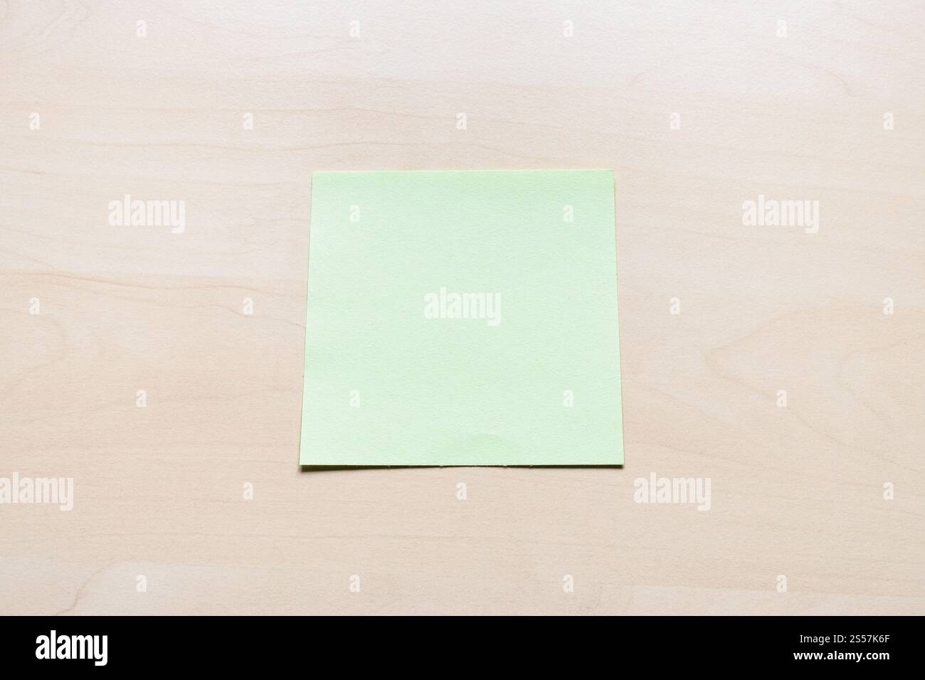 Draufsicht auf ein leeres grünes Blatt Notizpapier auf hellbraunem Holzbrett Stockfoto