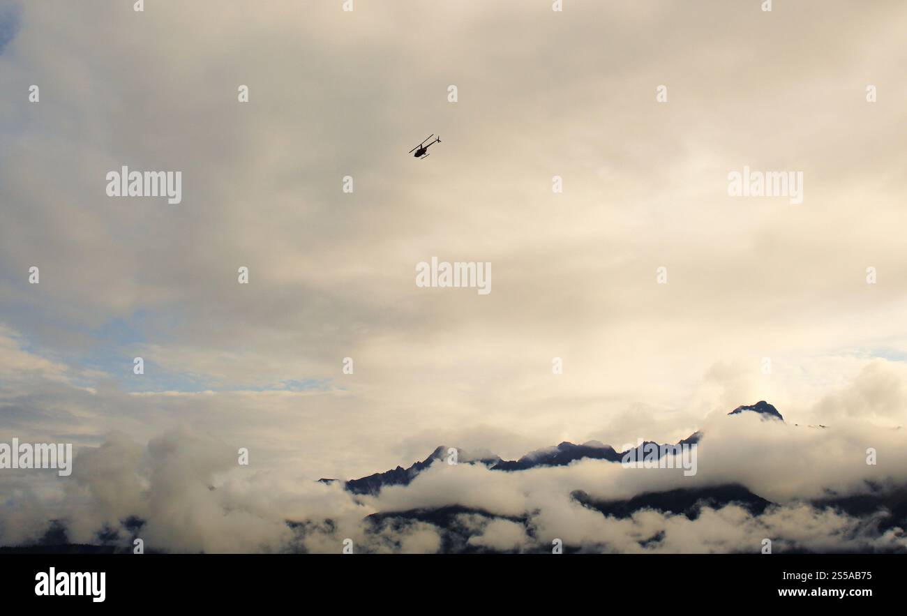 Ein Hubschrauber fliegt durch die dichte Wolkendecke über die Berge im dichten Nebel in Alaska, USA. Stockfoto