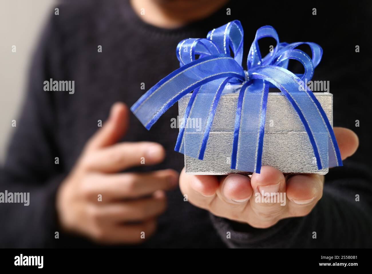 Geschenk geben, Mann Hand hält eine Geschenkbox in einer Geste des Gebens. Verschwommener Hintergrund, Bokeh-Effekt Stockfoto