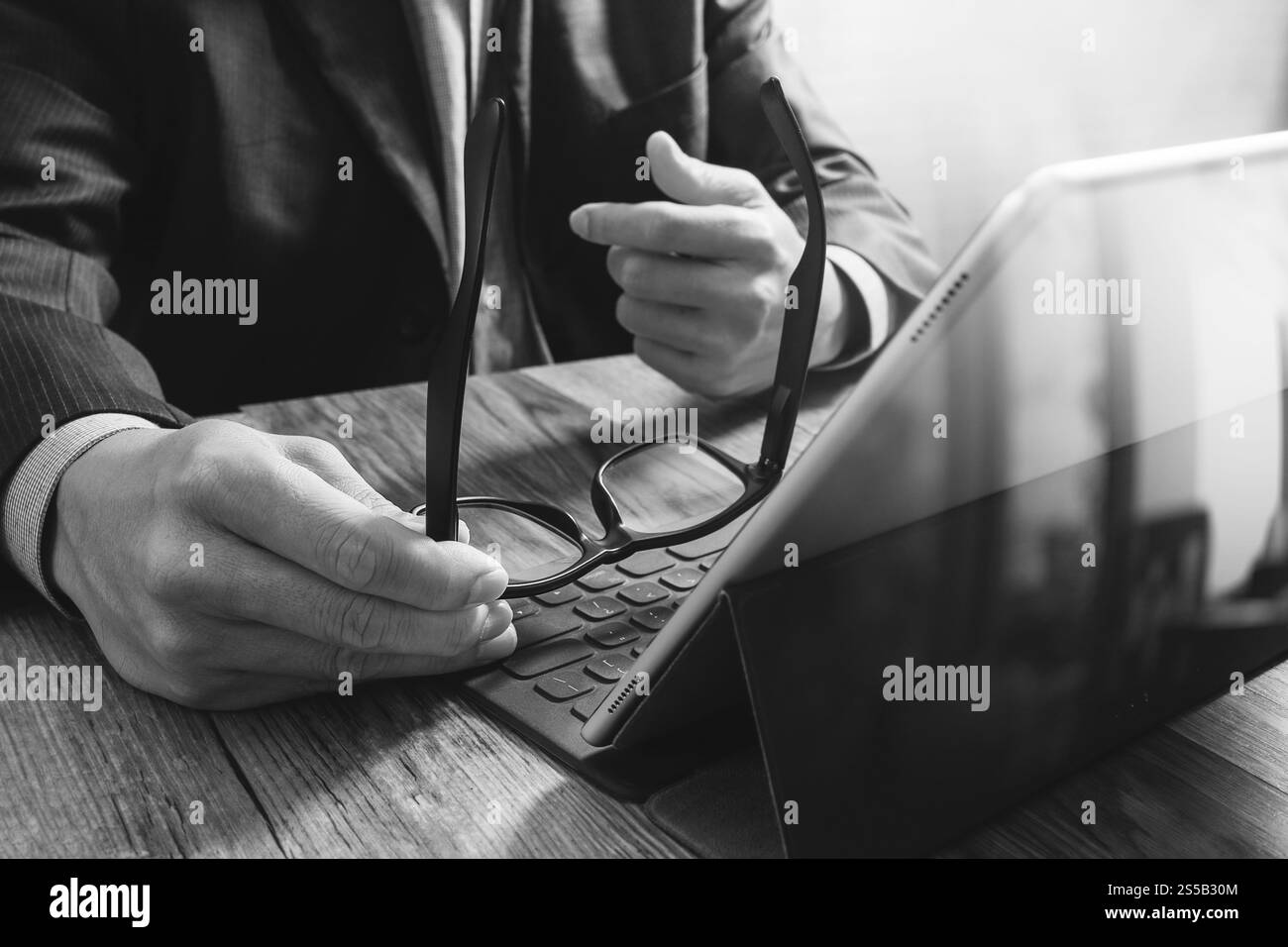 Erfolg Geschäftsmann Hand mit Brillen, digital-Tablette Docking-smart-Tastatur auf Holz Schreibtisch, schwarz weiß Stockfoto