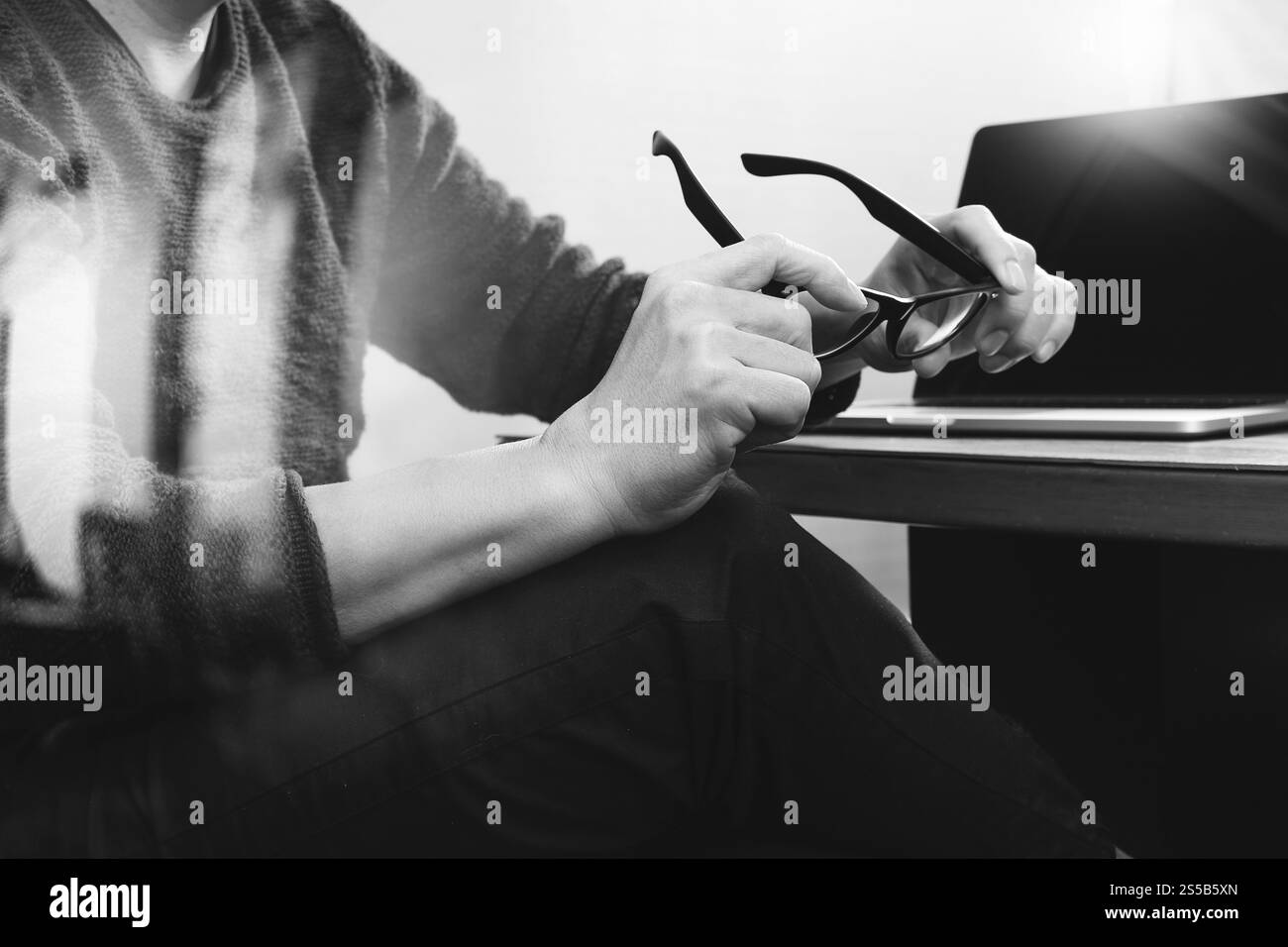 Der Designer der Website hält einen funktionierenden Computer mit Brille auf dem Holztisch, schwarz weiß Stockfoto
