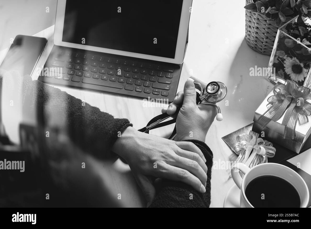 Geschenk geben, Arzt Hand mit Kreditkarte und Hand mit Geschenk. Geschenkelieferung, Überraschung, Laptop und Smartphone auf dem Schreibtisch, schwarz weiß Stockfoto