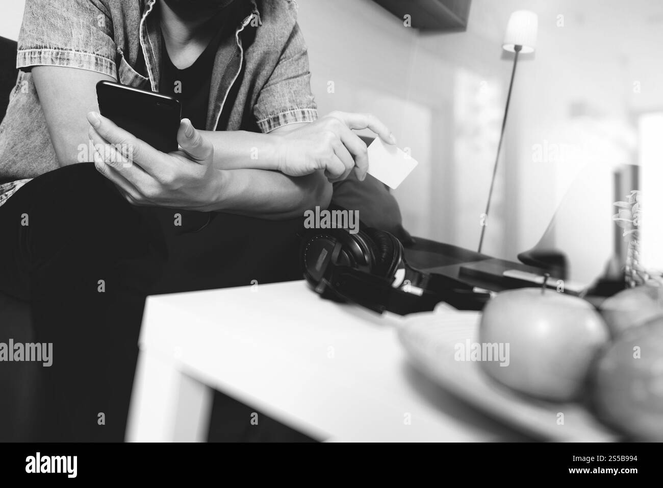 junger Mann sitzt auf Sofa Einkaufen online mit Smartphone hält Musik hören mit Kopfhörern Kreditkarte auf seiner Hand im Wohnzimmer, Omni Stockfoto