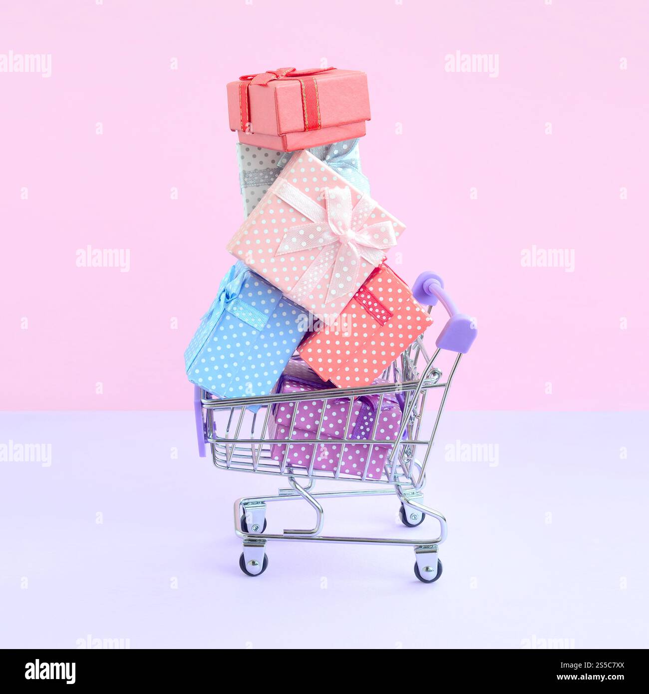Viele bunte Geschenkboxen im Supermarkt-Einkaufswagen auf violettem Hintergrund. Geschenke für Winterferien. Geschenkboxen für Winterferien in Stockfoto