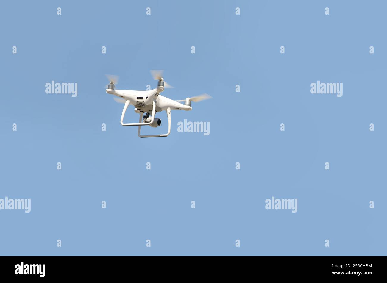 Große weiße Drohne, die in einem hellen wolkenlosen blauen Himmel schwebt, Funksteuerhubschrauber mit tragbarer Videokamera-Versorgung. Große weiße Drohne, die in A schwebt Stockfoto