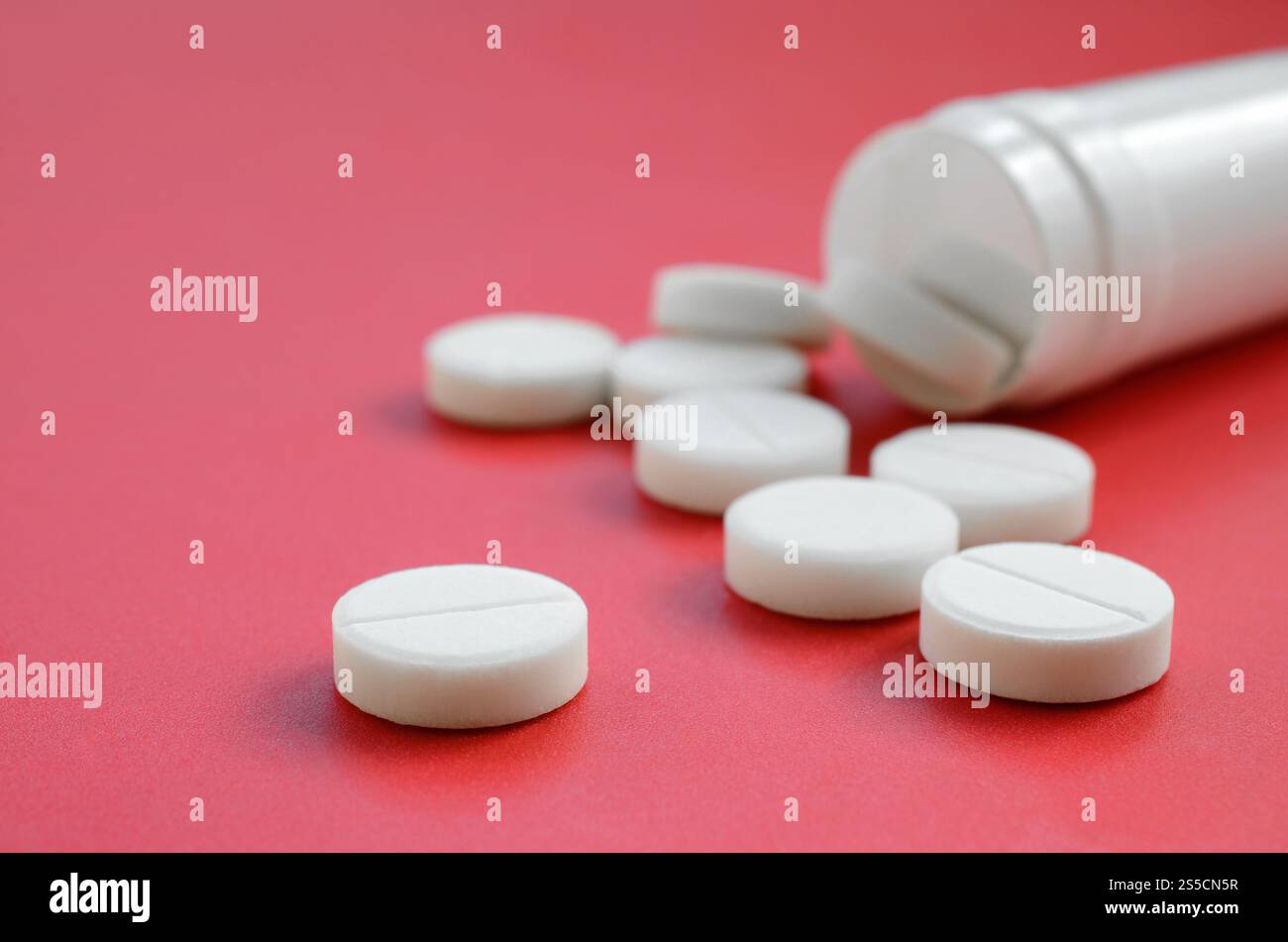 Mehrere weiße Tabletten fallen auf der roten Oberfläche aus dem Kunststoffbehälter. Hintergrundbild zu medizinischen und pharmazeutischen Themen Stockfoto