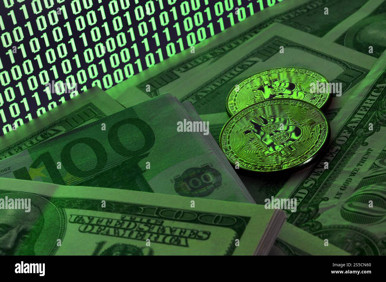Zwei Bitcoins liegen auf einem Stapel von Dollarscheinen auf dem Hintergrund eines Monitors, der einen Binärcode aus hellgrünen Nullen und eine Einheit auf einem schwarzen zeigt Stockfoto