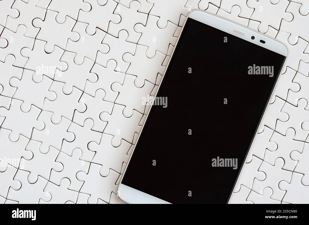 Eine moderne grosse Smartphone mit Touchscreen liegt auf einem weißen Puzzle im zusammengebauten Zustand Stockfoto
