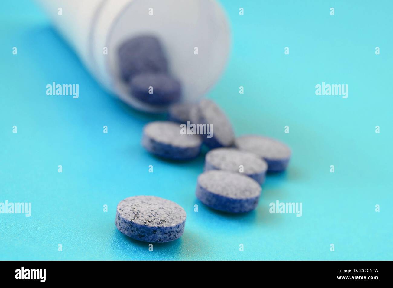 Mehrere graue Tabletten fallen aus der Kunststoffbehälter auf der blauen Fläche. Hintergrundbild über medizinische und pharmazeutische Themen Stockfoto