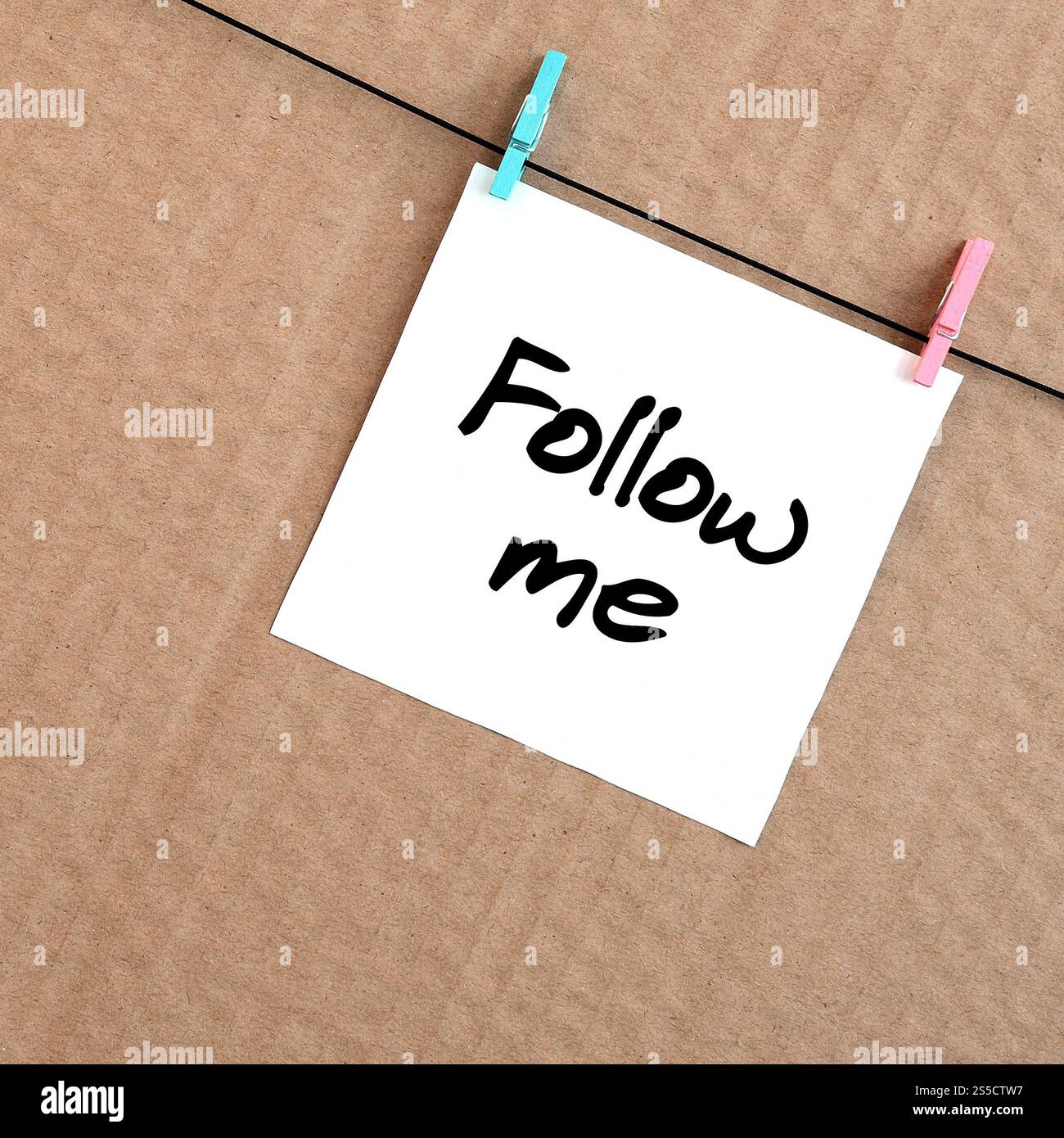 Folgen Sie mir. Die Notiz ist auf einem weißen Aufkleber angebracht, der mit einer Wäscheklammer an einem Seil auf einem Hintergrund aus braunem Karton hängt Stockfoto