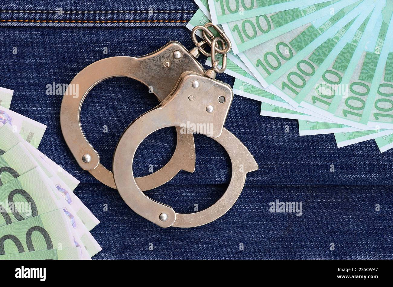 Der Fan von vielen Euro-Scheinen und Polizeihandschellen ist auf einer dunklen Jeansfläche. Hintergrundbild Stockfoto