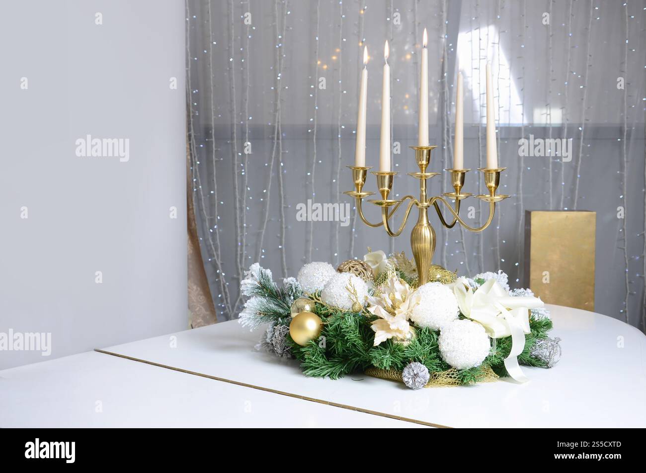 Neujahrsdekorationen und ein goldener Kerzenleuchter mit brennenden Kerzen stehen auf der Oberfläche eines weißen Flügels Stockfoto
