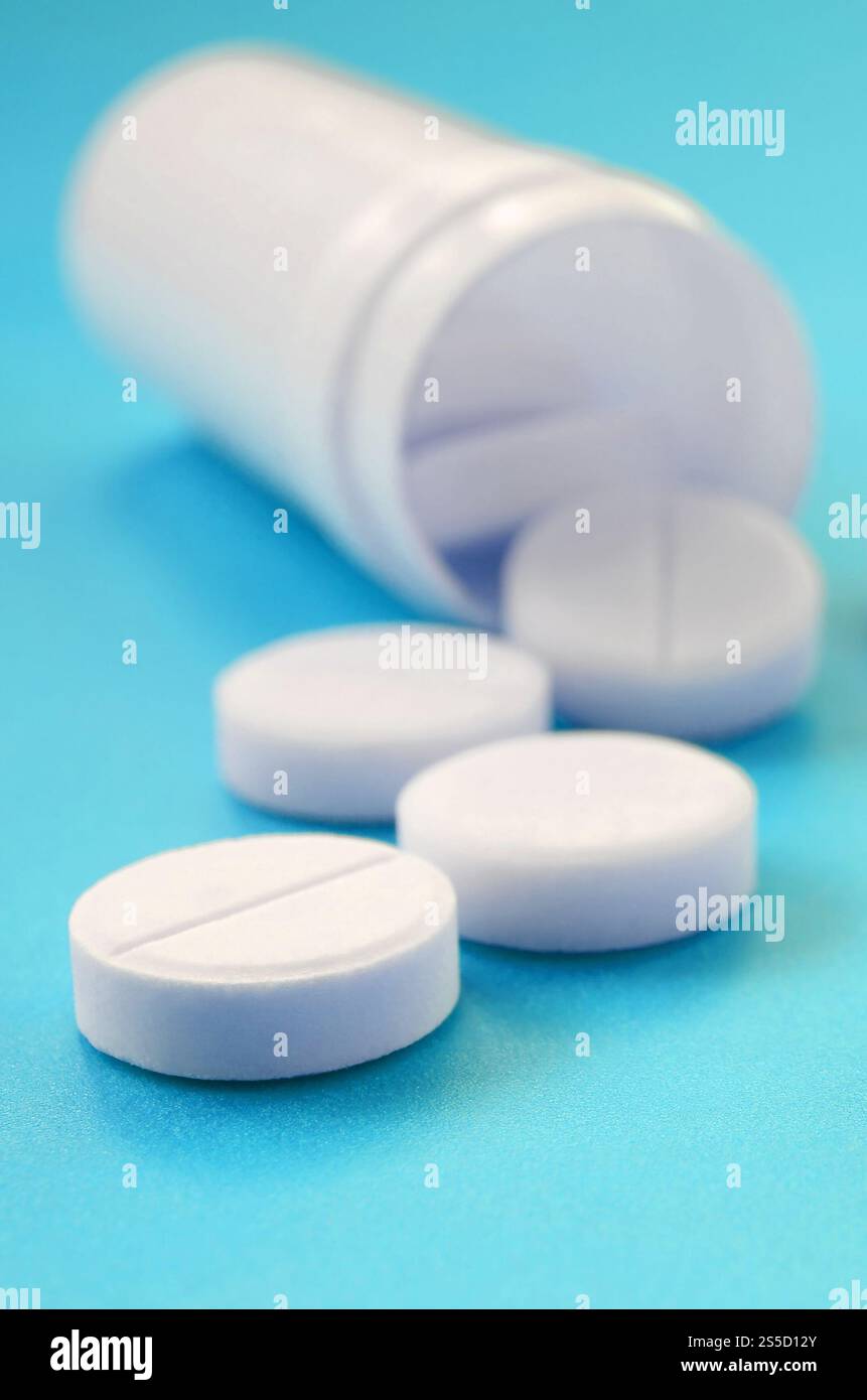 Mehrere weiße Tabletten fallen aus der Kunststoffbehälter auf der blauen Fläche. Hintergrundbild über medizinische und pharmazeutische Themen Stockfoto
