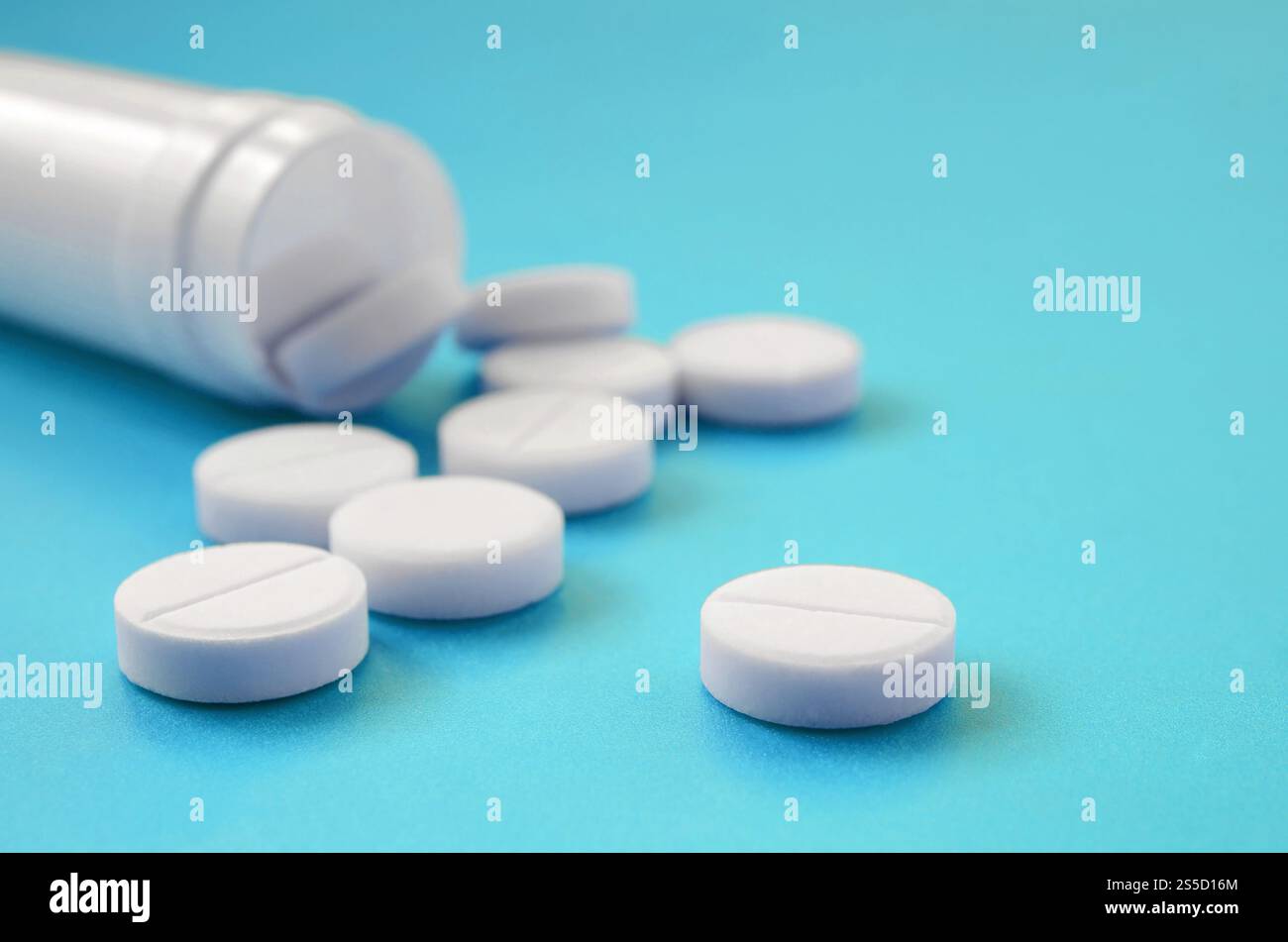 Mehrere weiße Tabletten fallen aus der Kunststoffbehälter auf der blauen Fläche. Hintergrundbild über medizinische und pharmazeutische Themen Stockfoto