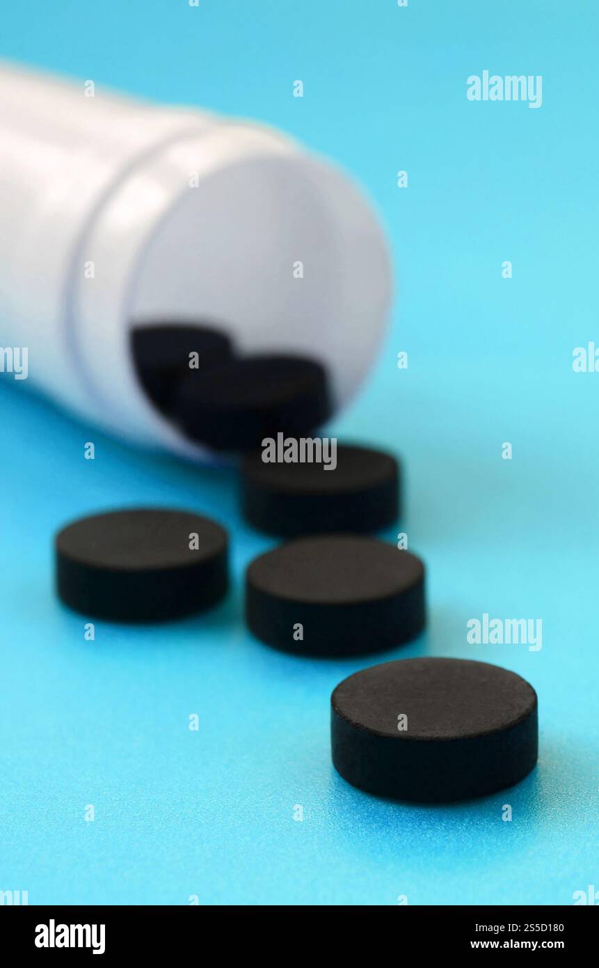 Mehrere schwarze Tabletten fallen aus der Kunststoffbehälter auf der blauen Fläche. Hintergrundbild über medizinische und pharmazeutische Themen. Aktivkohle Stockfoto